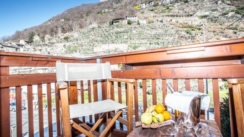 Balcon avec vue sur les vignes, chaises et table dressée avec une bouteille de vin mousseux de la Vallée d'Aoste